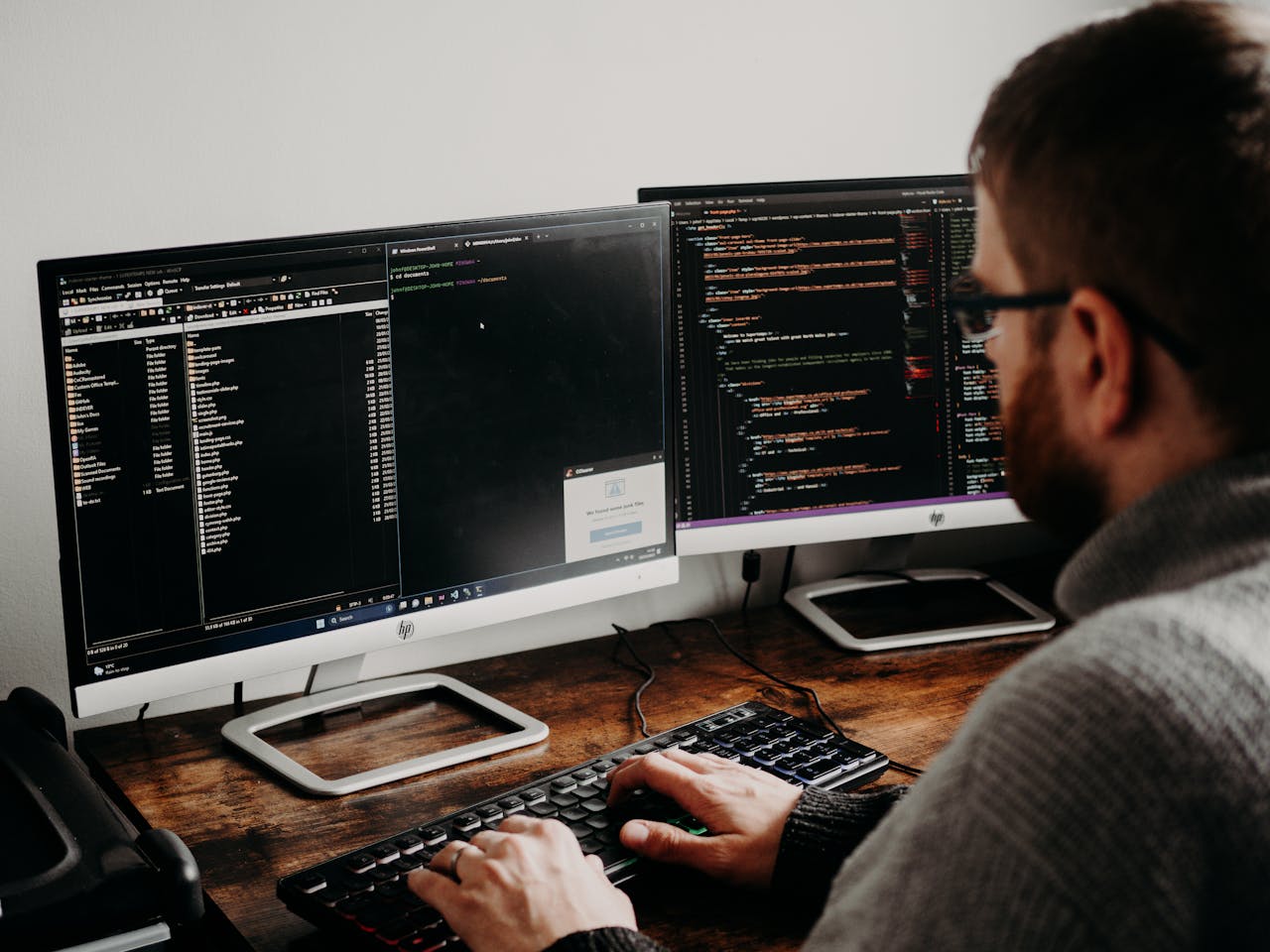 Home Software developer typing code on dual monitors at a wooden desk.